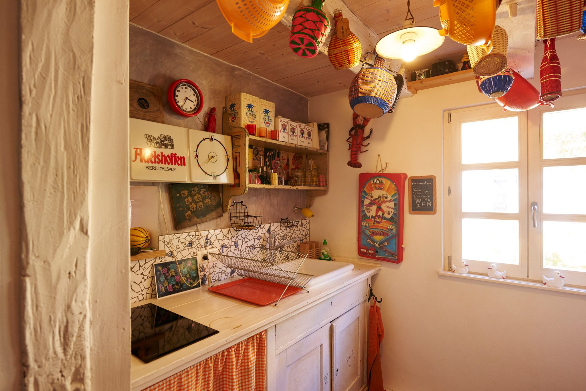 A kitchen with a white countertop, a red clock, and various kitchen items on shelves.