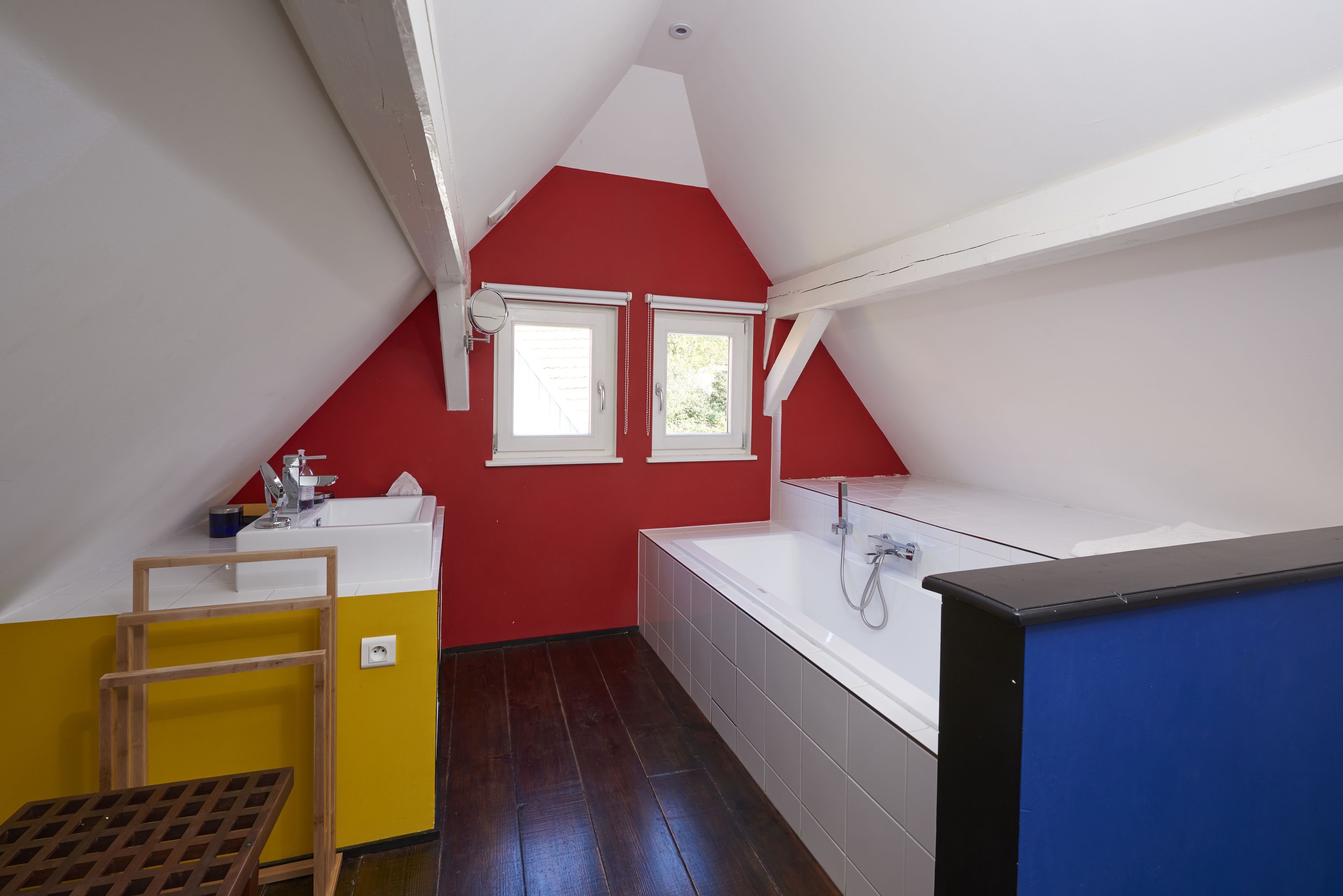 Une petite salle de bain aux couleurs vives, avec un mur rouge, des éléments d’équipement blancs et un plafond en pente.
