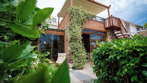 Una casa con fachada de ladrillo, terraza de madera y escalera que lleva a un balcón.