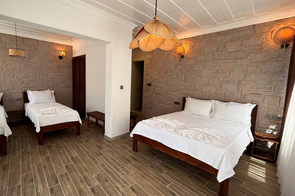 A hotel room with three beds, wooden flooring, stone walls, and a hanging light fixture.