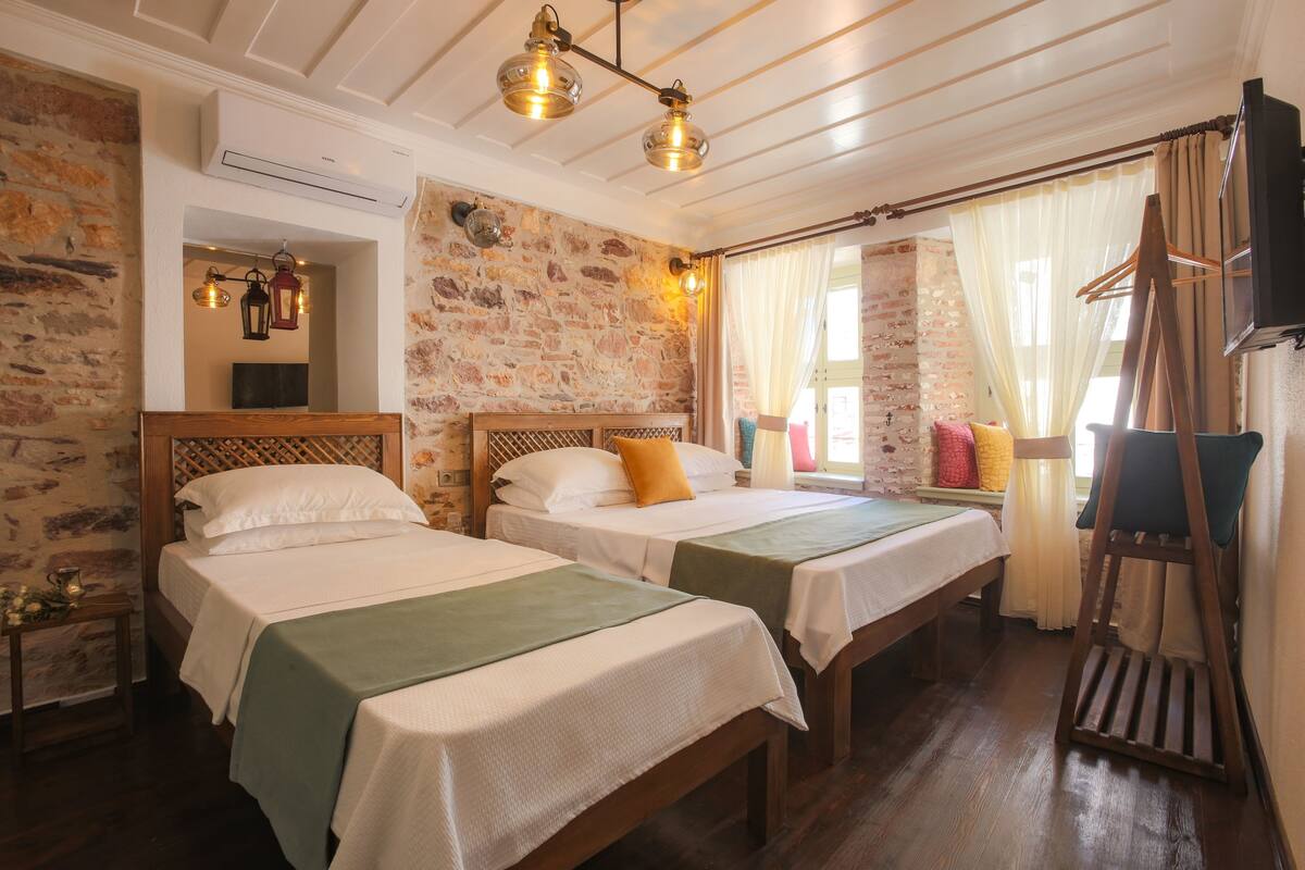 A room with two beds, a wooden ladder, a hanging light fixture, and a brick wall.