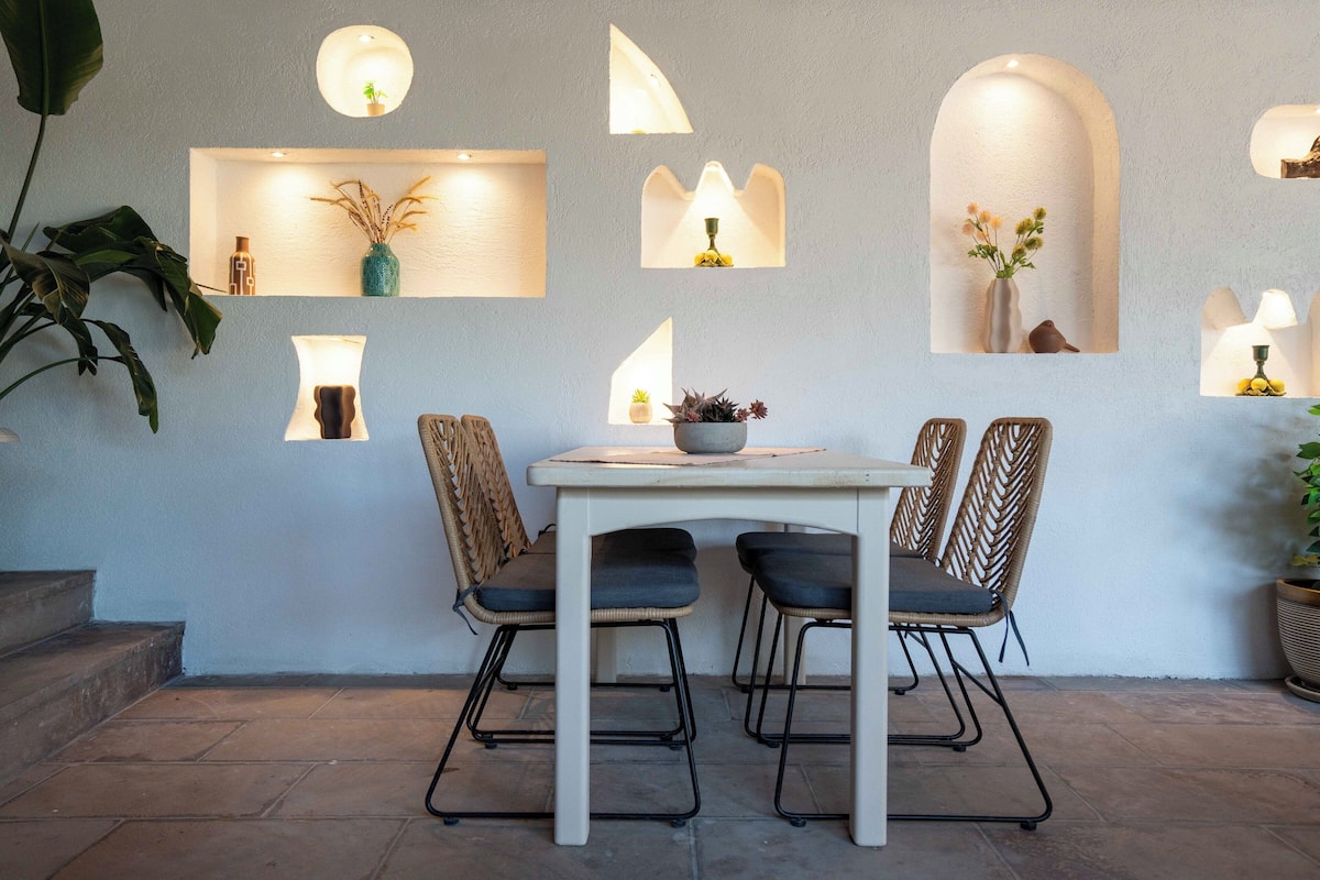 A dining area with a table and chairs, a potted plant, and wall-mounted lighting fixtures.