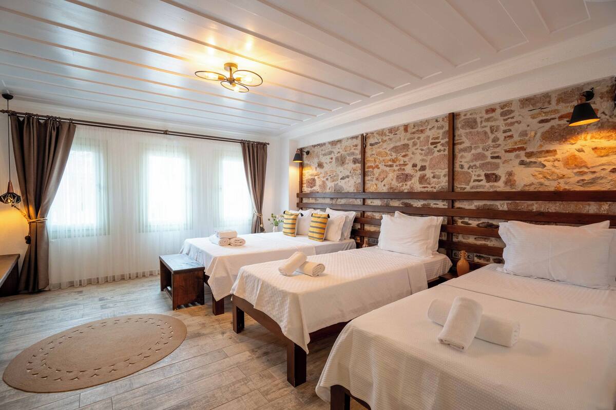 A hotel room with two beds, a stone accent wall, and a wooden ceiling.
