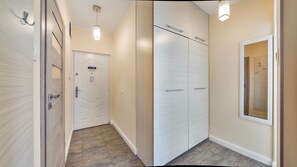Un pasillo con una puerta blanca, un armario con pomo y un espejo en la pared.