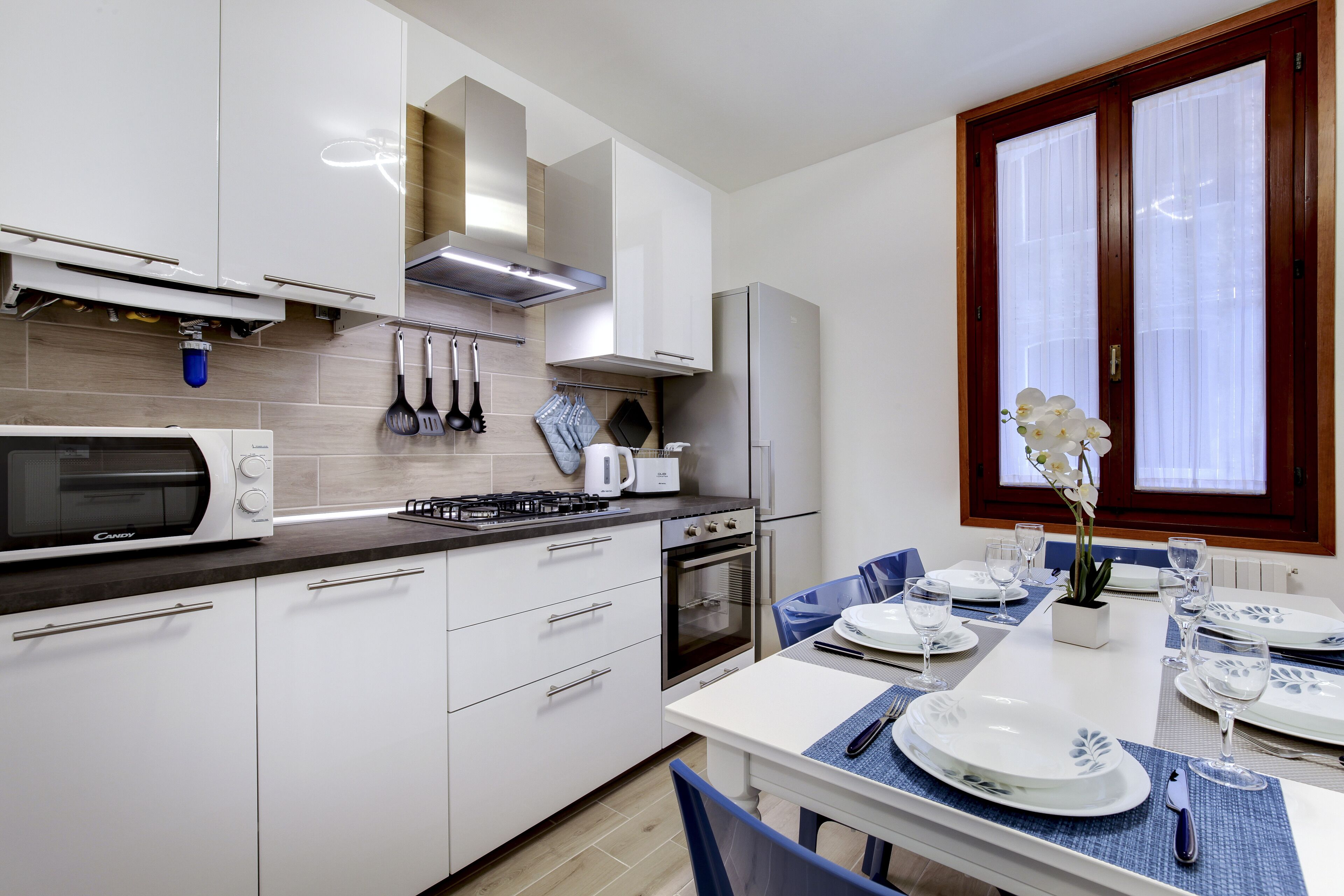 A modern kitchen with white cabinets, a microwave, stove, oven, and a dining area with a table set for two.