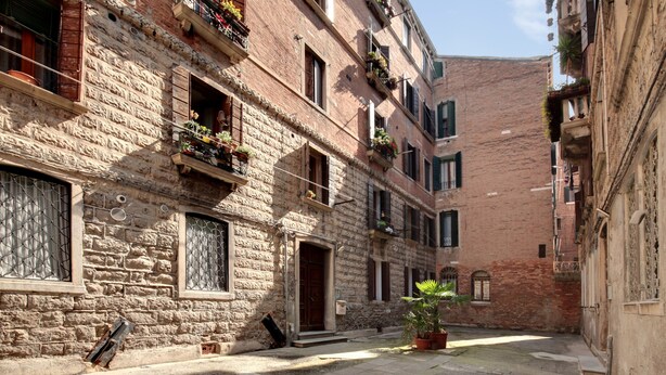 Une rue étroite bordée d’immeubles en pierre, de balcons ornés de plantes et d’une petite cour intérieure.