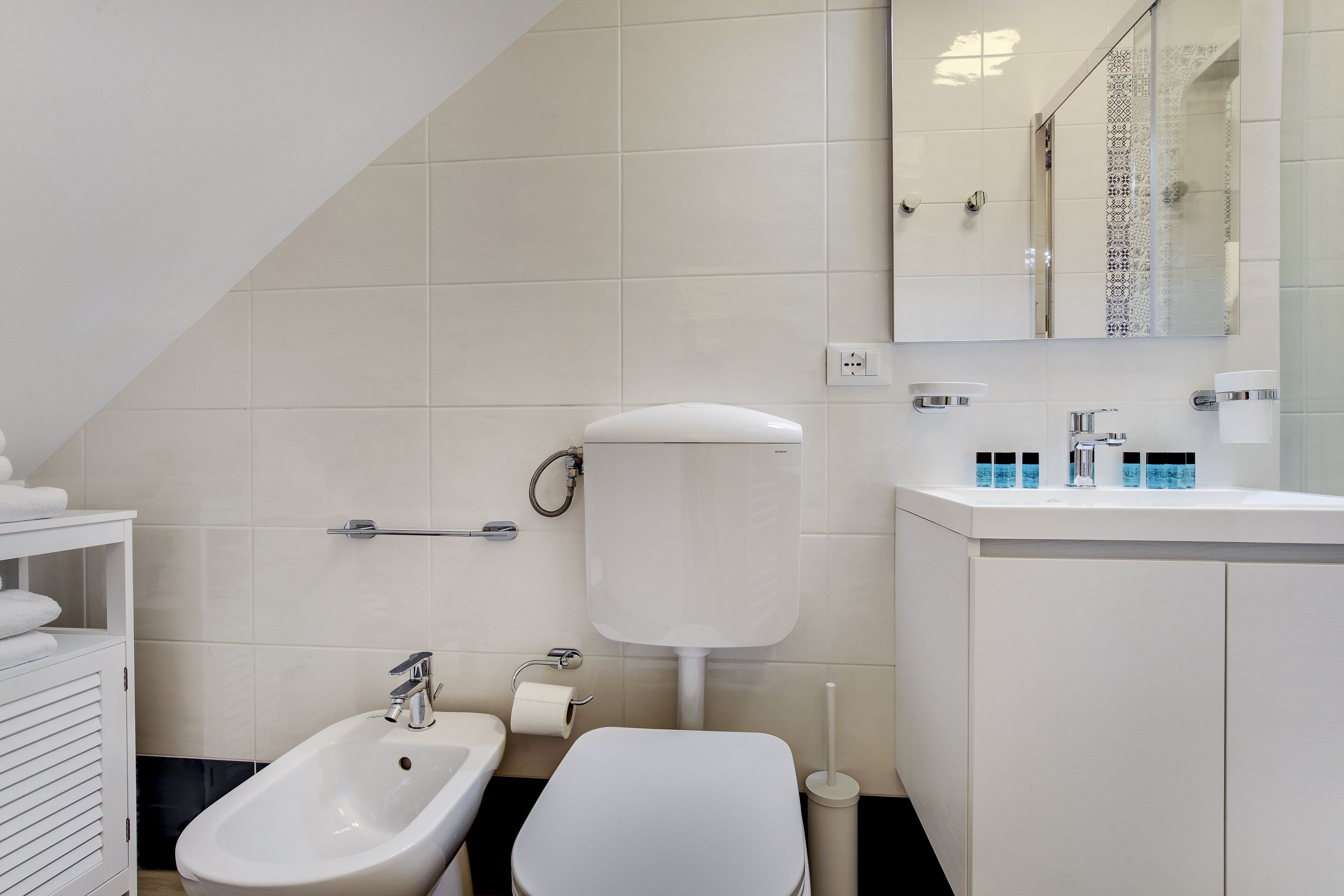 Un baño moderno con un bidé, inodoro, lavabo y espejo.