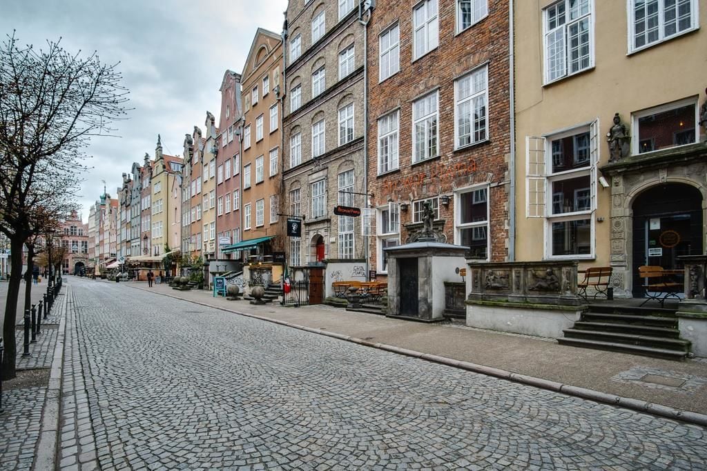 A cobblestone street lined with historic buildings, some with visible signage and architectural details.