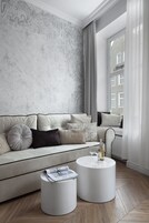 A modern living room with a sofa, two white side tables, and a window with curtains.