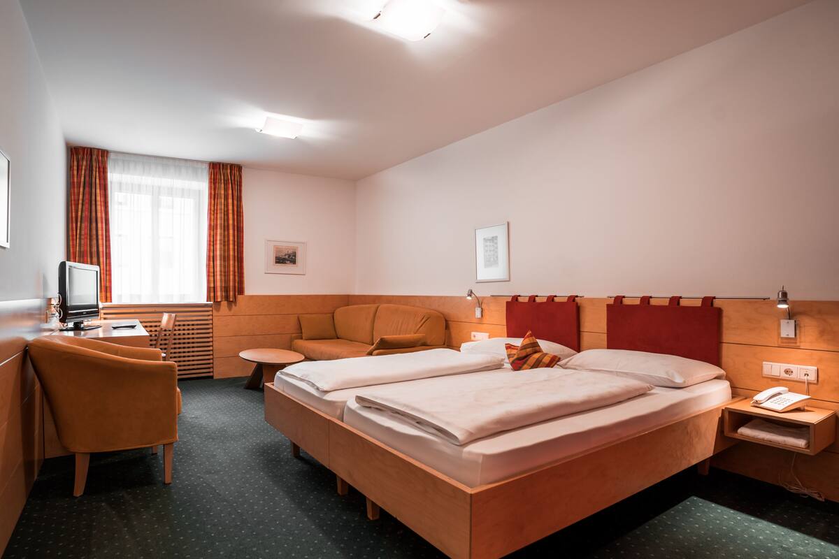 A hotel room with a bed, a desk, a chair, a small table, and a television.