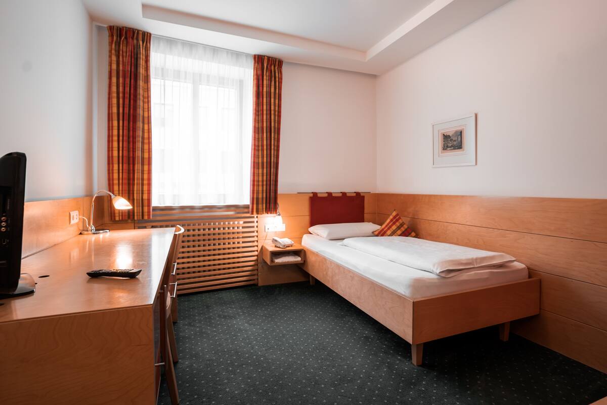 A hotel room with a bed, a desk, a chair, a lamp, and a window with curtains.