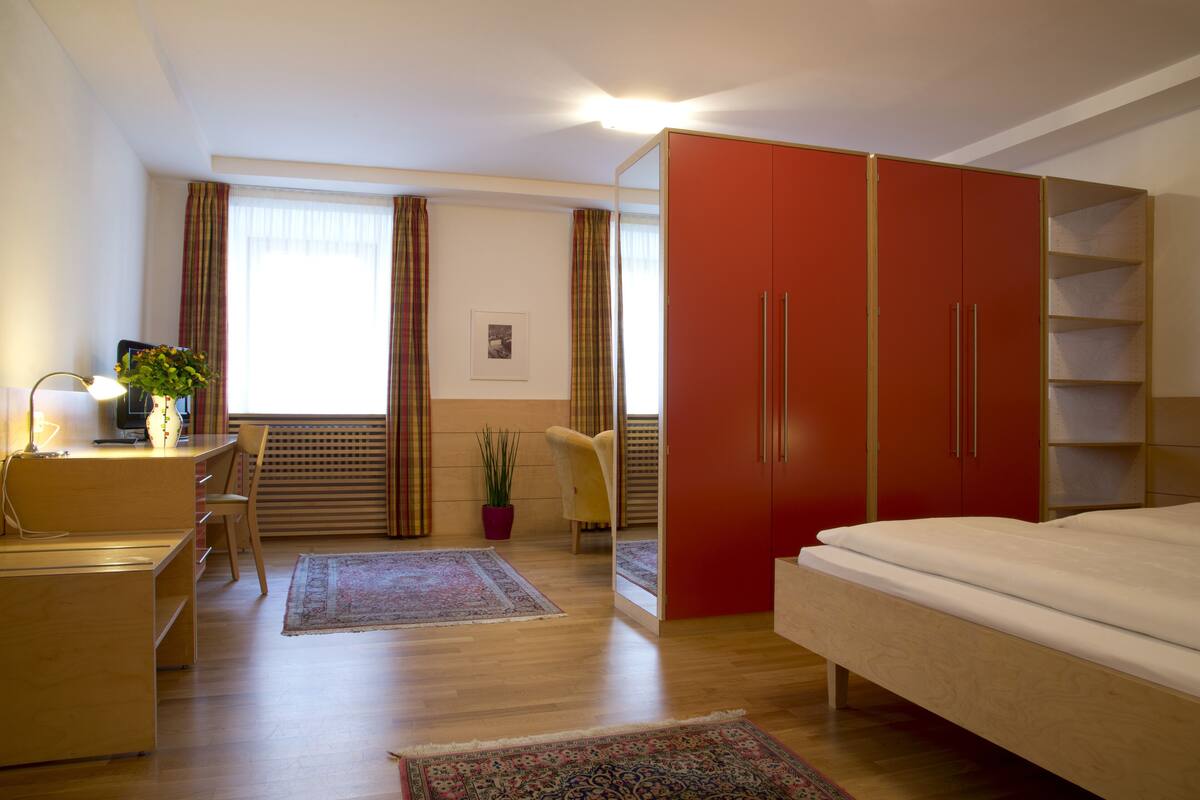 A modern bedroom with a bed, a desk, a chair, and a wardrobe.