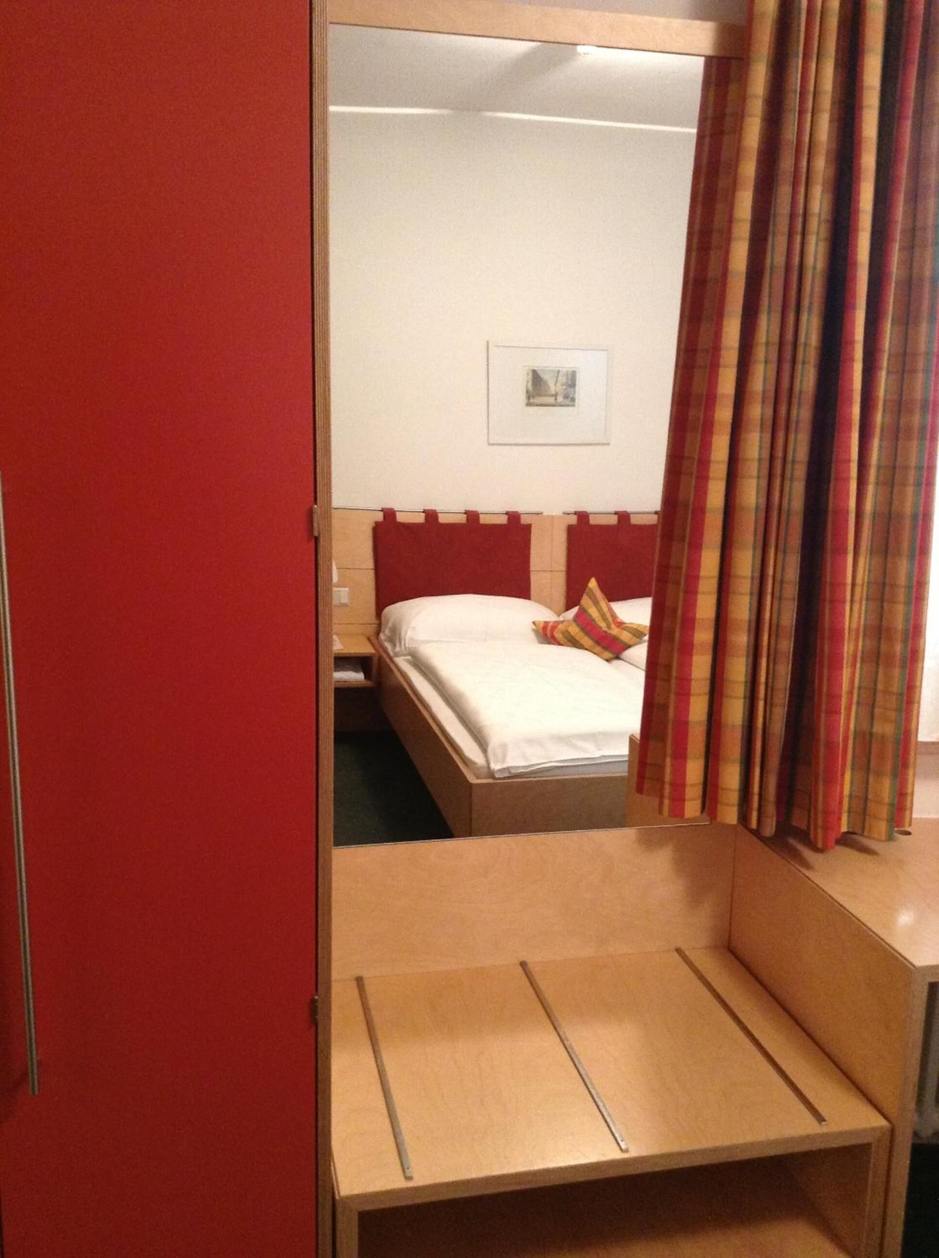 A hotel room with a bed, a small table, and a mirror.
