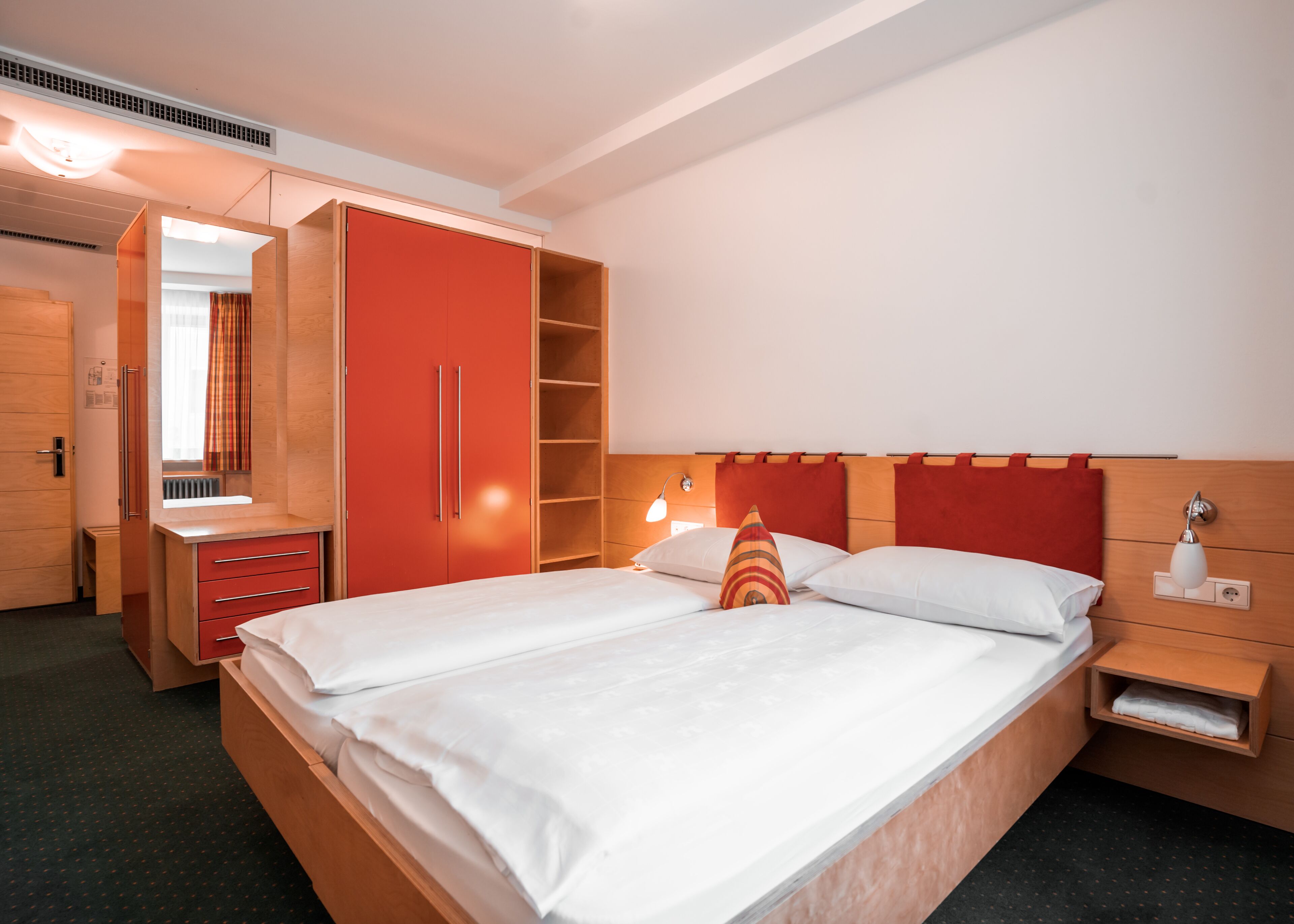 Une chambre d’hôtel avec un grand lit, une armoire avec un miroir, une table de chevet et une petite table de nuit.