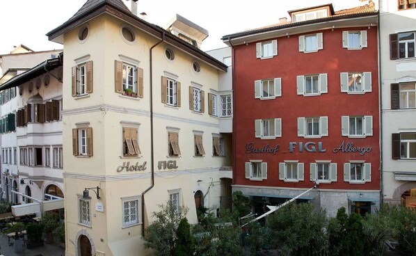 Un hotel con fachada clásica europea, que presenta múltiples ventanas con contraventanas y un letrero llamativo que dice "Hotel FIGL".