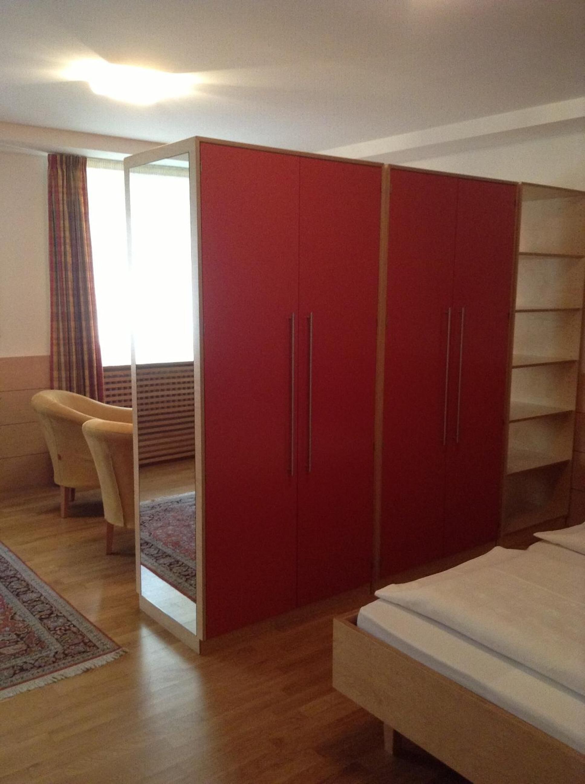 Un dormitorio con cama, un armario rojo, una silla y una ventana con cortinas.