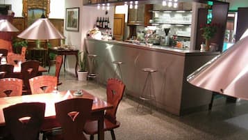 Zona de bar con taburetes, una barra y varias botellas. Se ven mesas y sillas en primer plano.