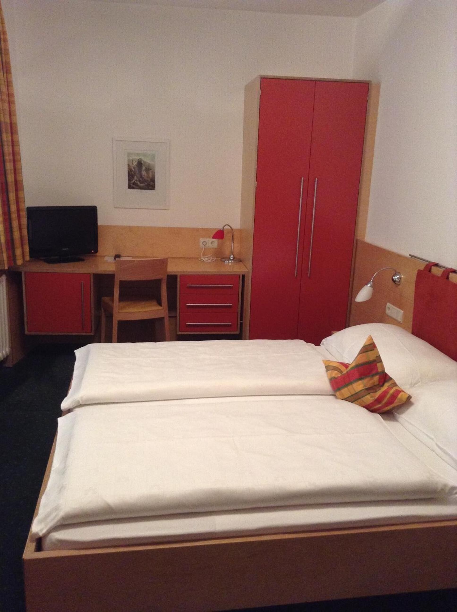 Una habitación de hotel con cama, escritorio, silla, televisor y armario.