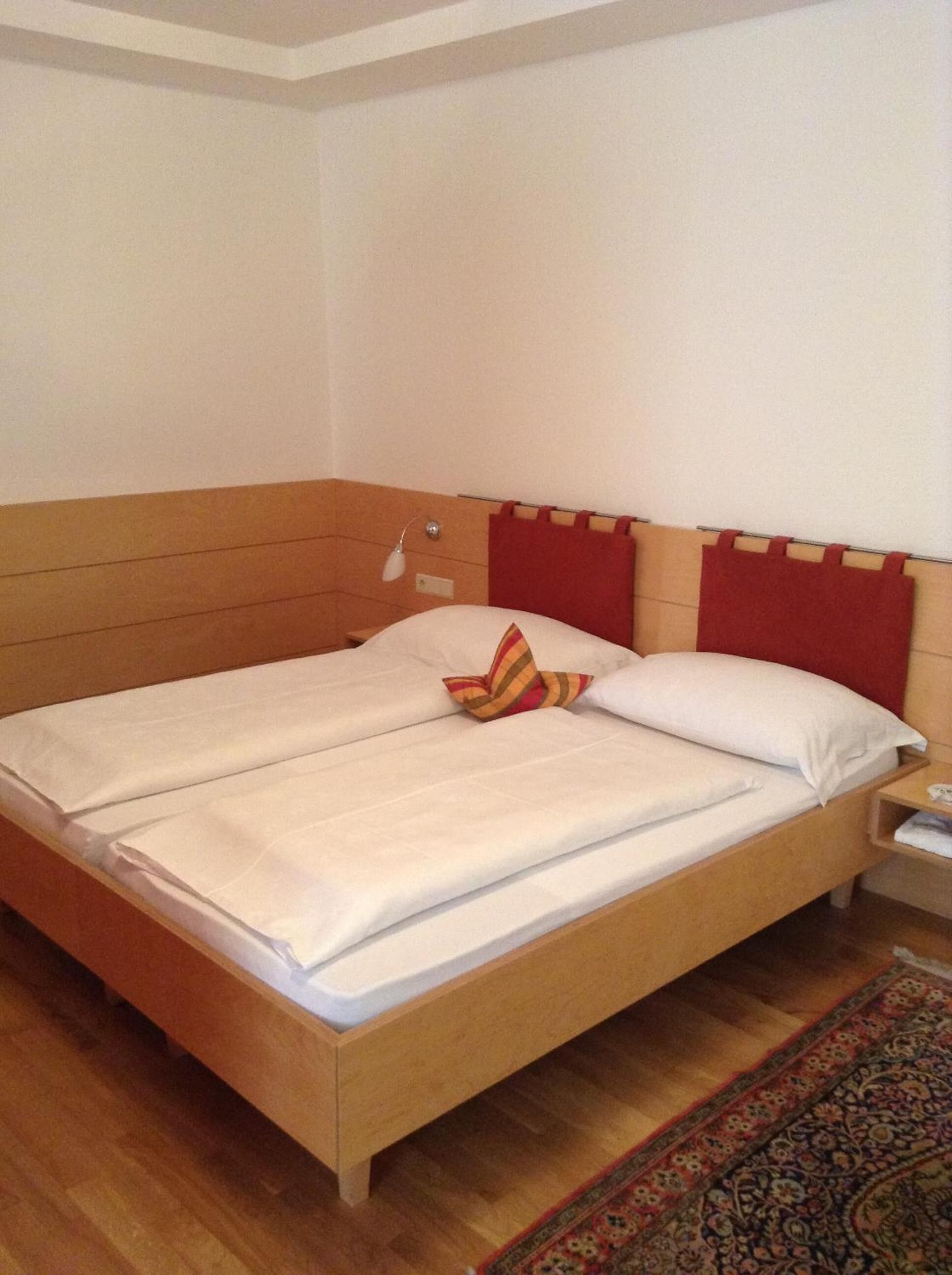 Cama bem arrumada com travesseiro listrado, cabeceira de madeira e mesa de cabeceira com abajur.
