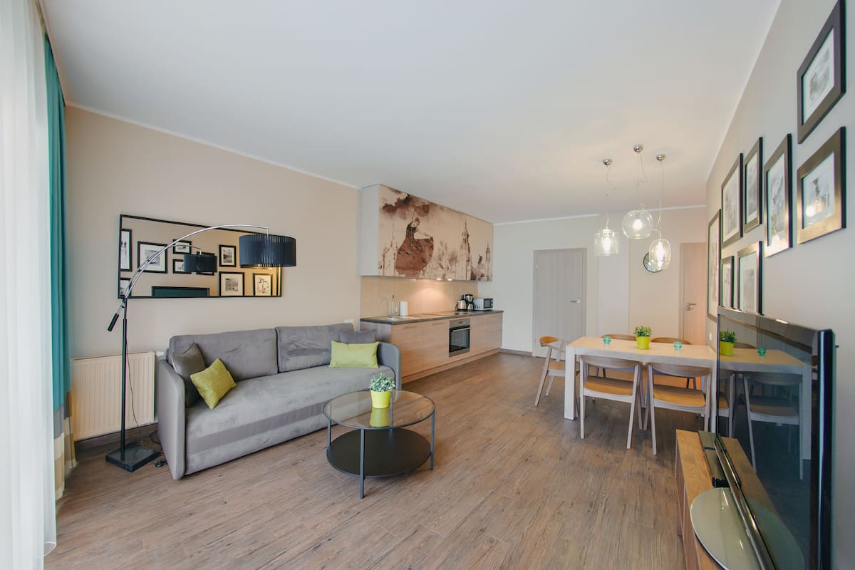 Un salon moderne avec un canapé gris, une table basse en verre et un coin repas comprenant une table et des chaises blanches.