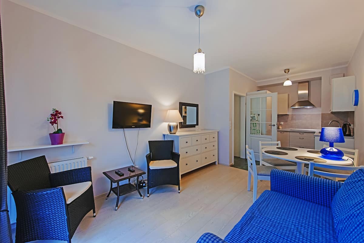 Un salon moderne comprenant un canapé, un téléviseur, une table à manger avec des chaises, un coin cuisine et une petite table avec une lampe.