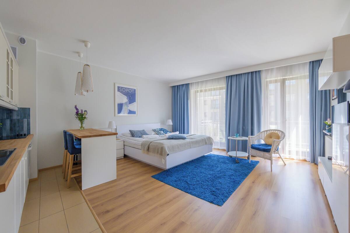 Une chambre d’hôtel moderne équipée d’un lit, d’un petit bureau, d’une chaise, d’une télévision et d’une grande fenêtre avec des rideaux.