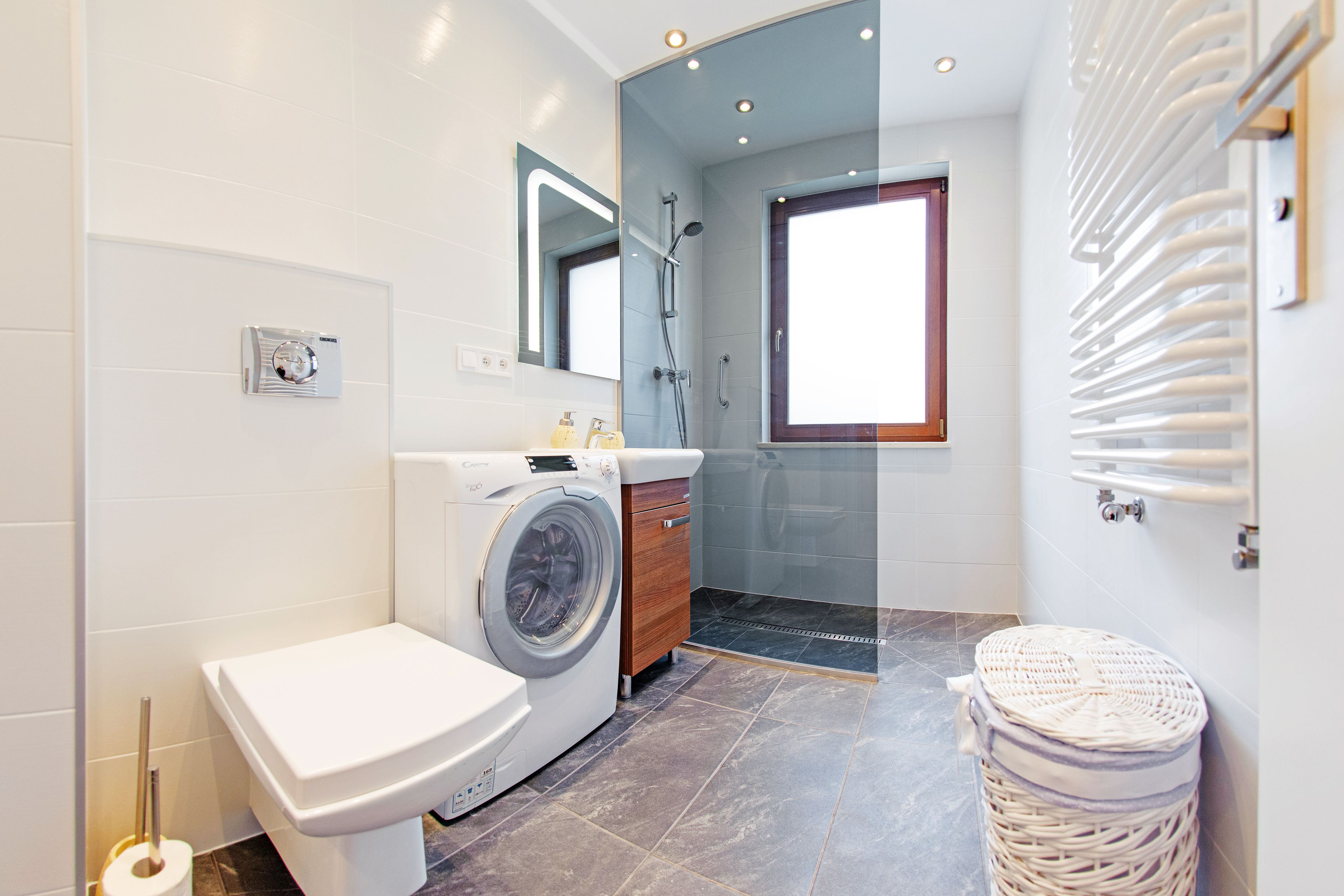 Een moderne badkamer met een wasmachine, toilet en douche.