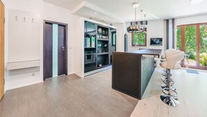 Une cuisine moderne dotée d’un îlot central, d’un coin repas avec des tabourets de bar et d’une grande fenêtre offrant une vue sur la verdure.