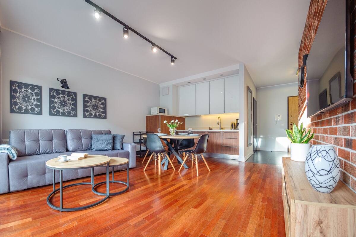Un salon moderne avec un canapé gris, deux petites tables rondes et un coin repas comprenant une table et des chaises.