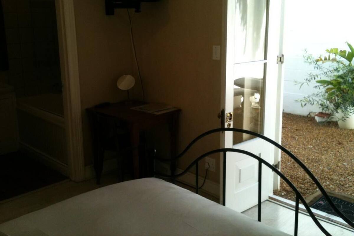Un dormitorio con cama, mesita de noche, lámpara y puerta que da a un balcón con vistas al exterior.