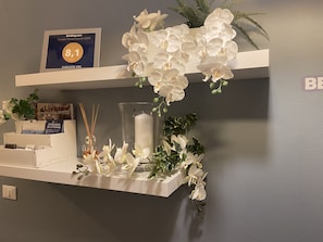 A hotel reception area with a framed award certificate, a white orchid arrangement, and a candle on a shelf. - Paradise Inn (Livorno)