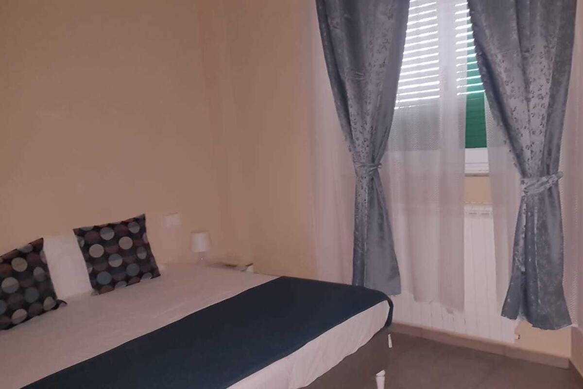 A bedroom with a bed, pillows, a nightstand, and a window with curtains.