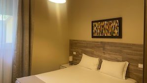 A hotel room with a bed, a nightstand, a lamp, a wall-mounted artwork, and a window with curtains. - Paradise Inn (Livorno)