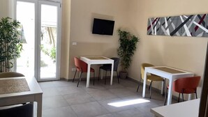 A modern living room with a flat-screen TV mounted on the wall, a large potted plant, and a dining area with two tables and four chairs. - Paradise Inn (Livorno)