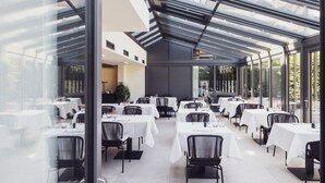 Un restaurant moderne aux murs de verre et au plafond haut, avec des nappes blanches et des chaises noires.