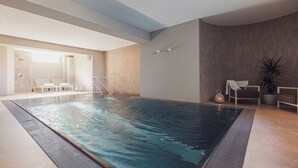 Une piscine intérieure à l’eau claire, entourée de chaises longues et agrémentée d’une plante en pot.