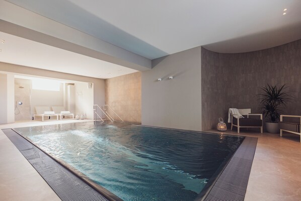 Una piscina interior con superficie de agua cristalina, rodeada de sillones de descanso y una planta en maceta.