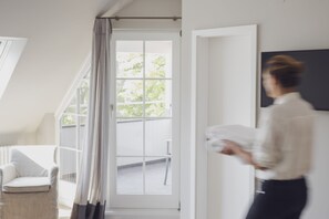 A room with a large window, a chair, and a person holding a white object. - Caraleon (Wasserburg am Bodensee)