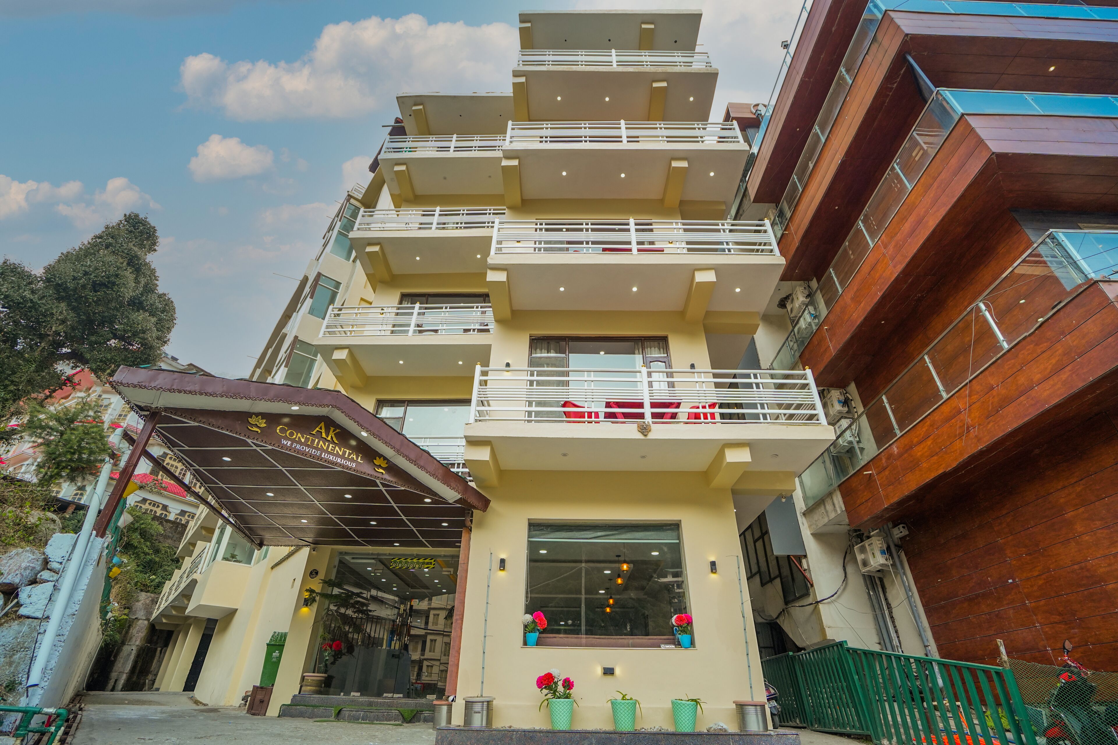 A multi-story hotel with balconies, a covered entrance, and potted plants.