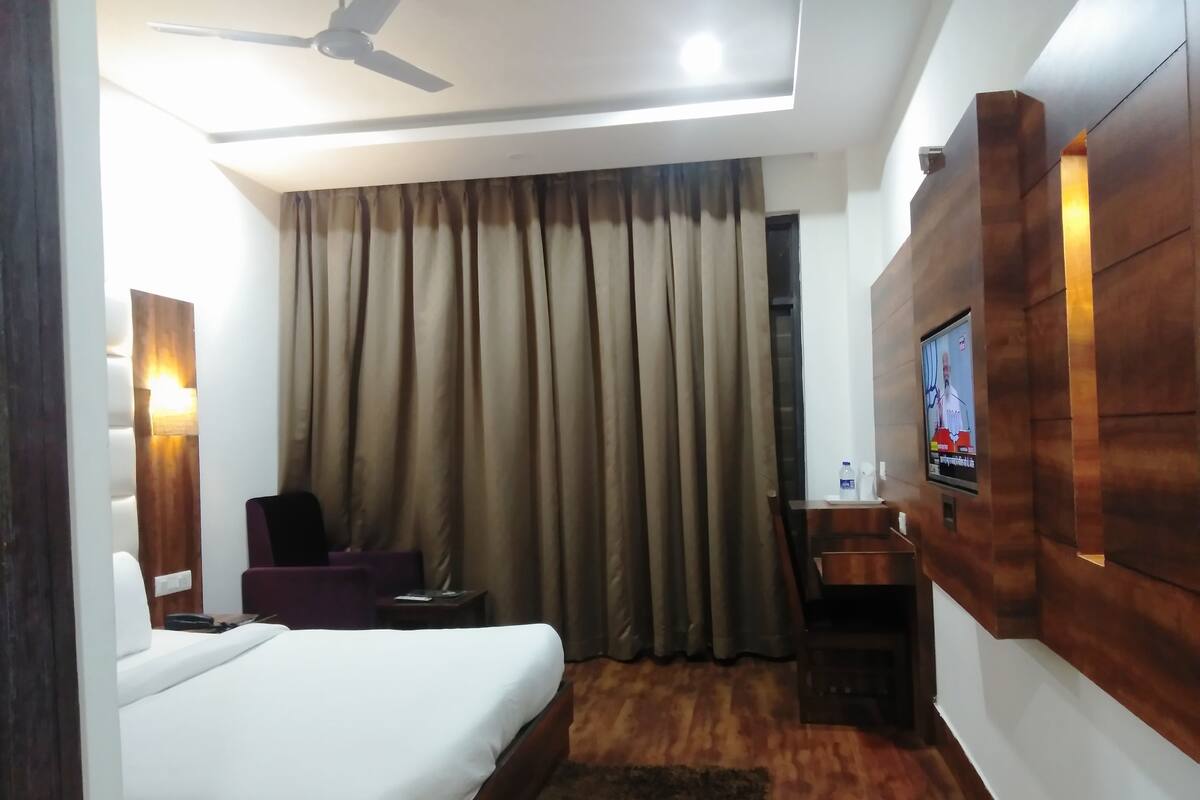 Una habitación de hotel con cama, escritorio, silla, televisor y ventilador de techo.