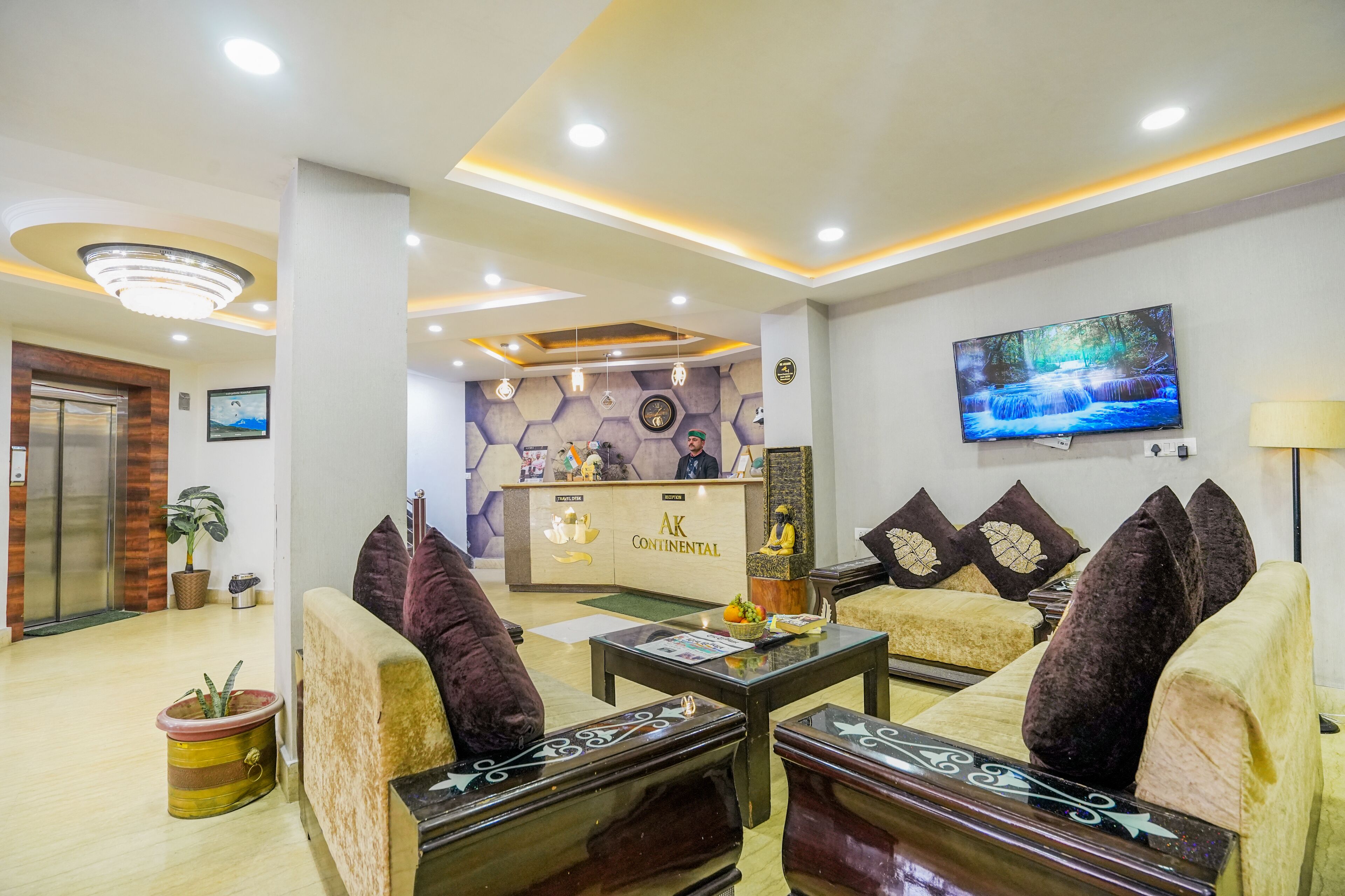 A hotel lobby with a reception desk, sofas, a coffee table, and a television on the wall.
