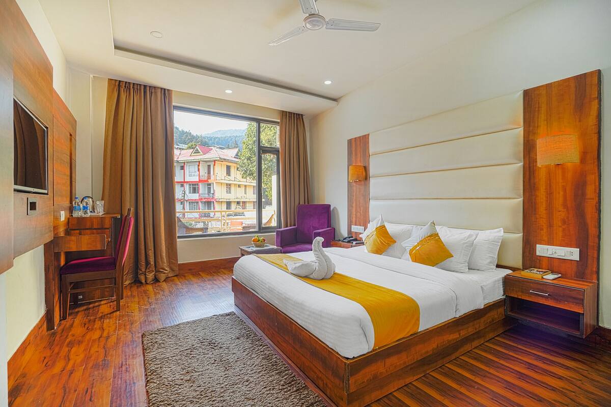 Habitación de hotel con una cama grande, un escritorio, una silla y vistas a edificios desde la ventana.