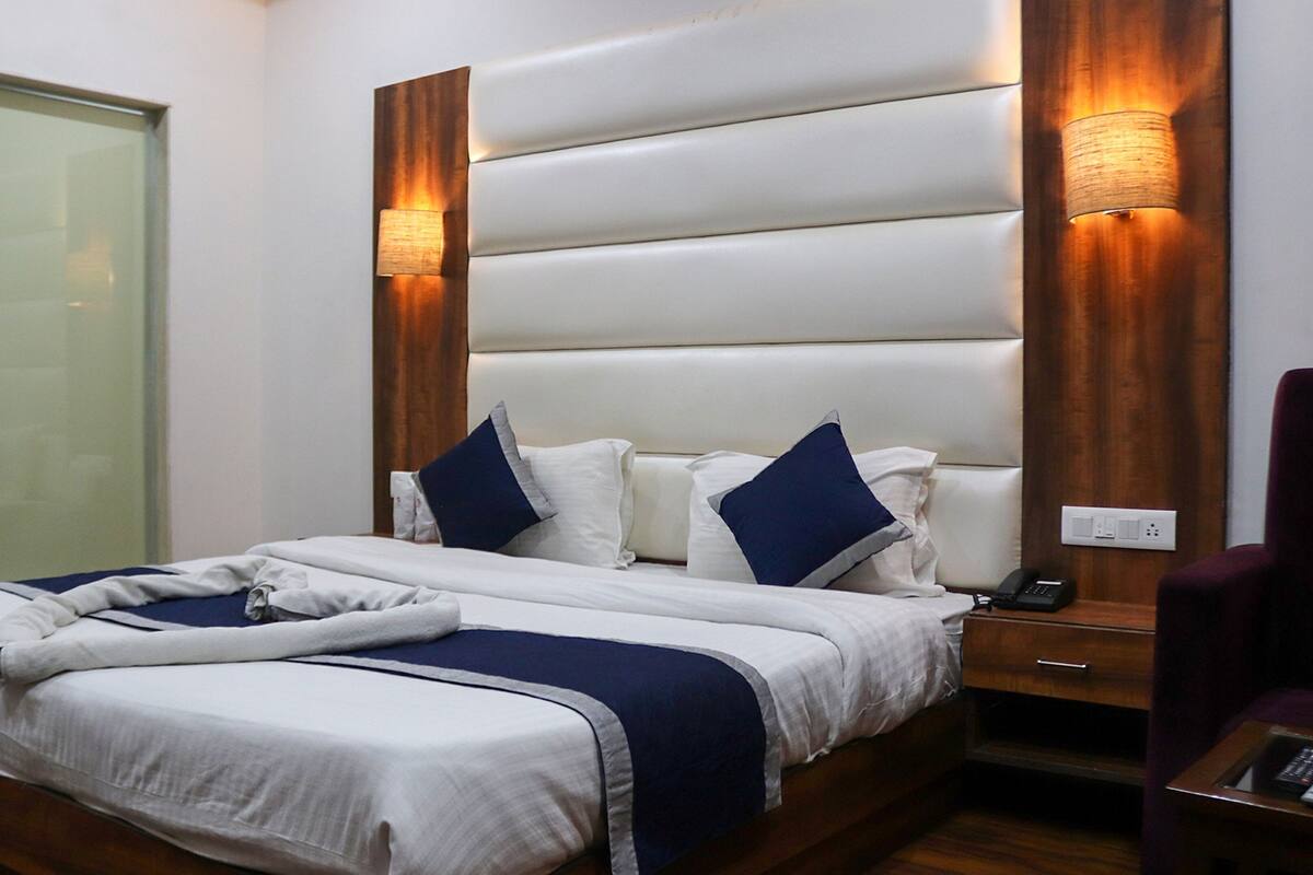Una habitación de hotel con una cama grande, mesitas de noche, una silla y un ventanal.