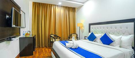 Quarto de hotel com cama, televisão, escrivaninha e cadeira.