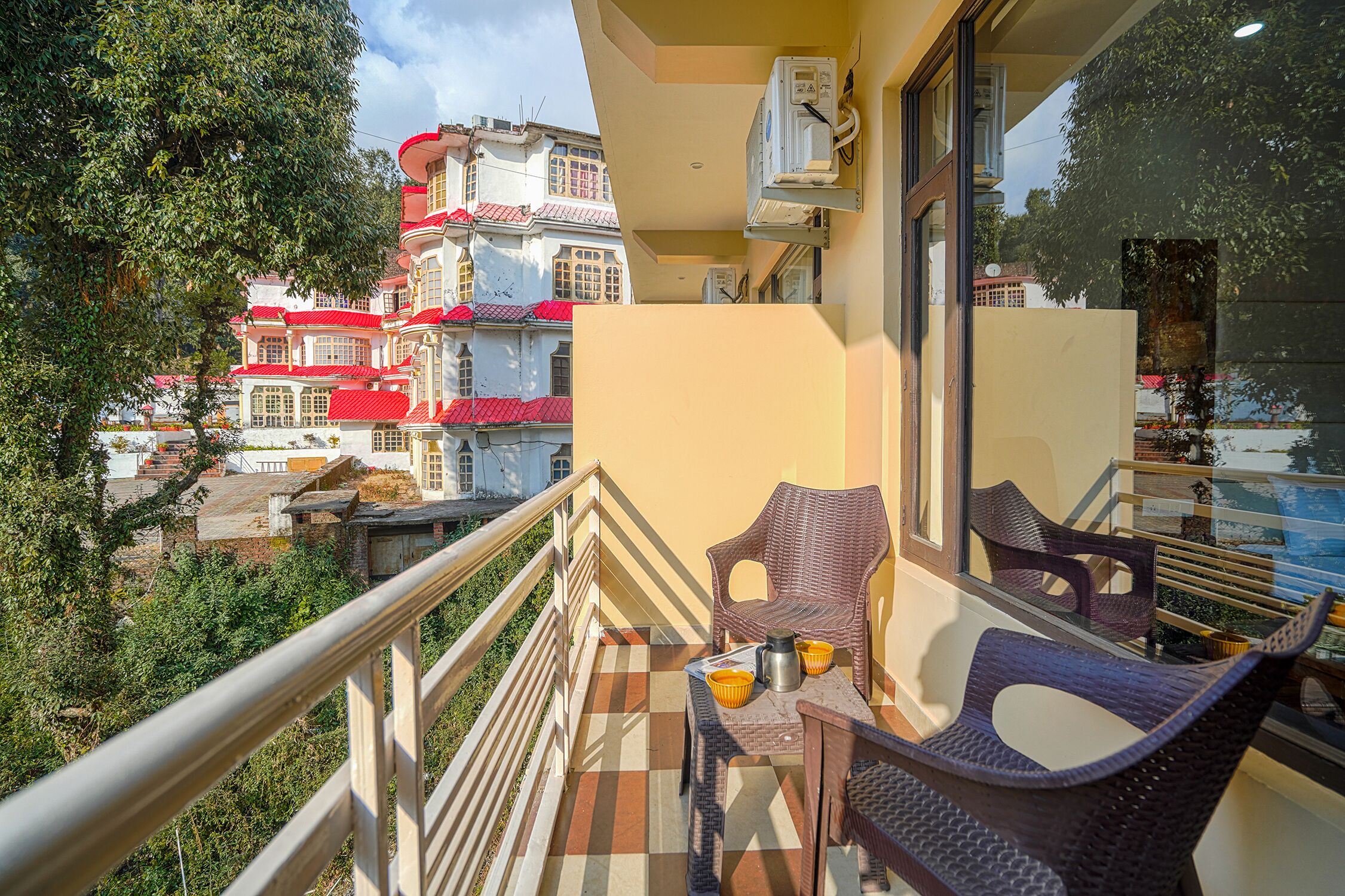 Un balcon agrémenté de meubles en osier, une table avec une tasse et un thermos, et une vue sur des bâtiments aux toits rouges.