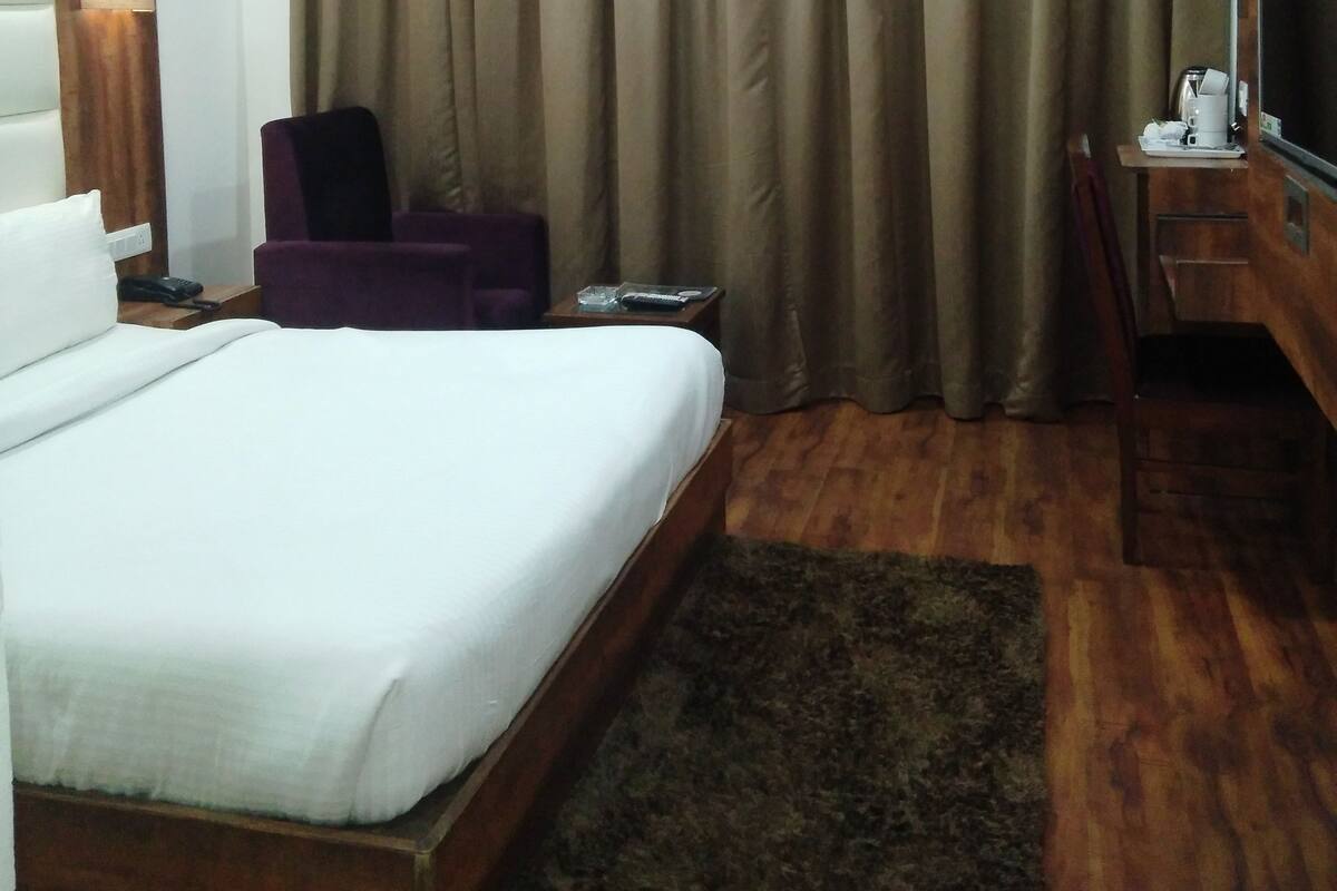 Habitación de hotel con cama, escritorio con televisor, silla, lámpara y ventilador de techo.