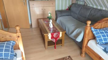 A cozy room with a wooden bed, a sofa, a small wooden table with a vase, and a wardrobe.