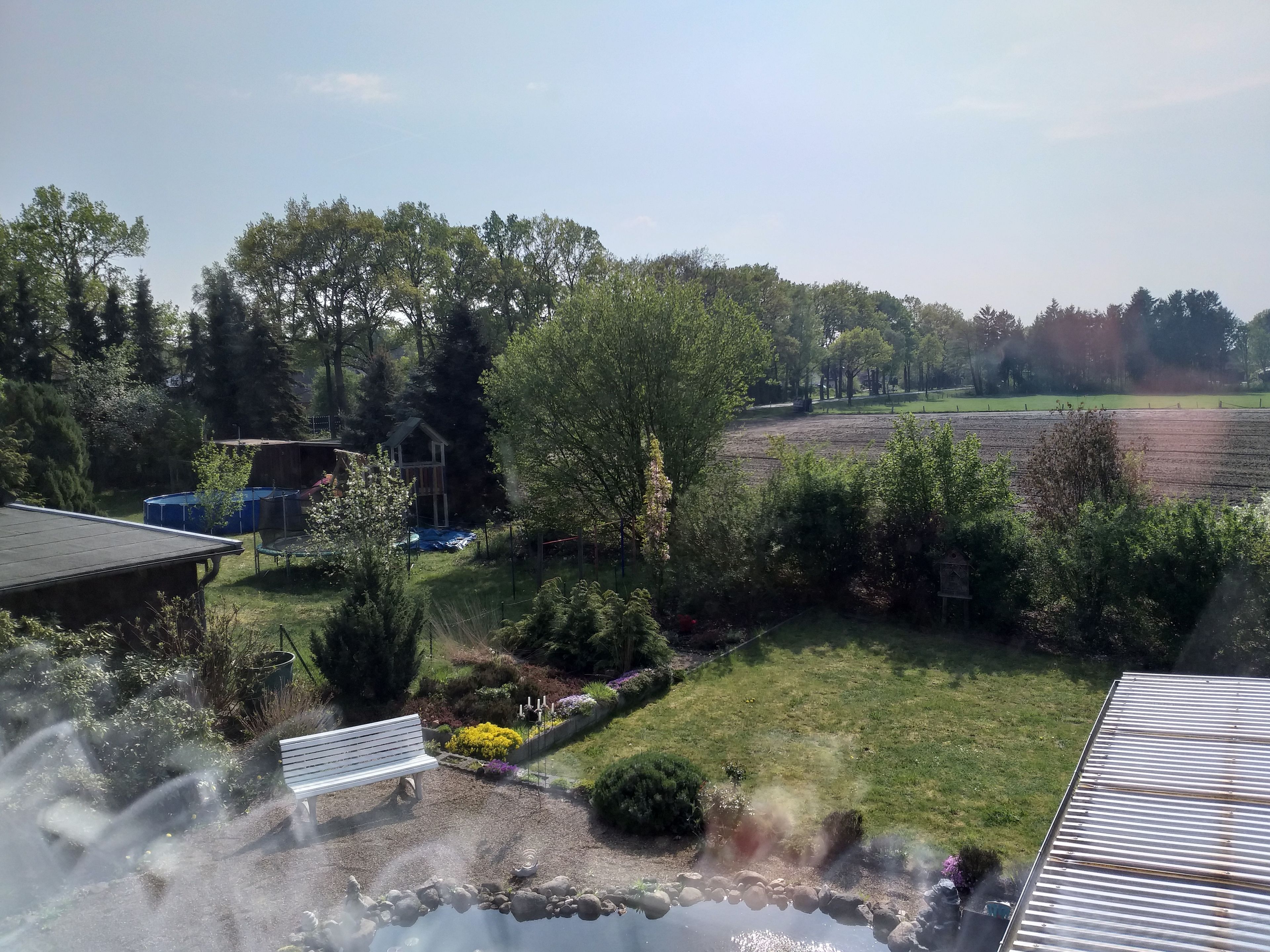 Una zona residencial con jardín, un estanque pequeño y un campo al fondo.