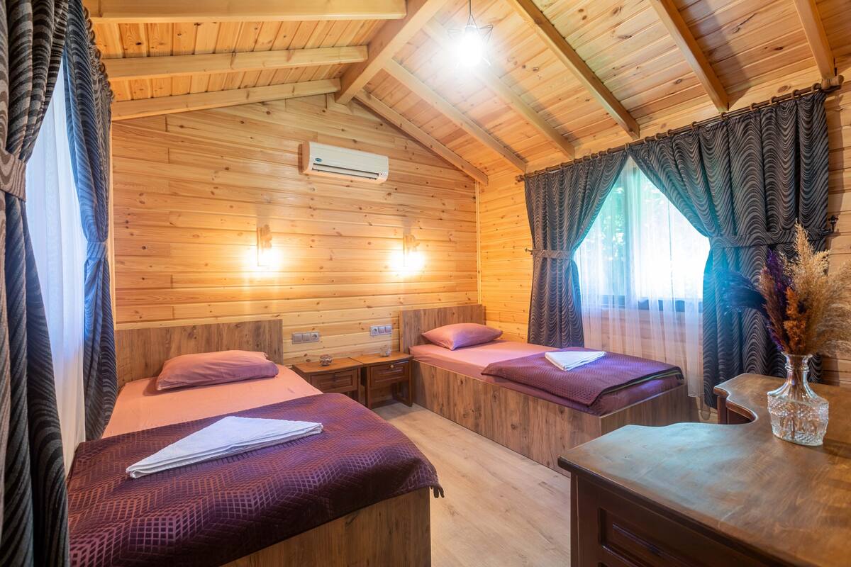 Eine Hütte mit zwei Holzbetten, einem Holztisch und einem Fenster mit Vorhängen.