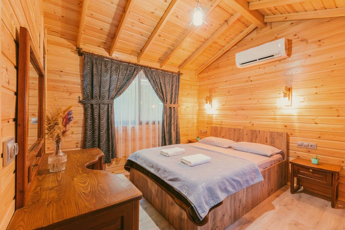 Ein Schlafzimmer einer Holzhütte mit einem Bett, einem Nachttisch, einer Kommode und einem Fenster mit Vorhängen.